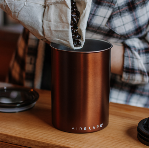 Airscape coffee canister in brushed copper, filled with whole beans on a wood counter